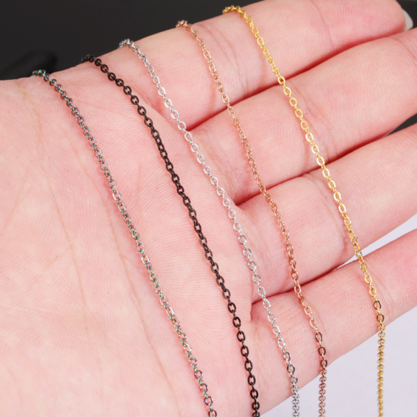 Stainless steel cross chains in silver, gold, black, and rose gold, held in hand.