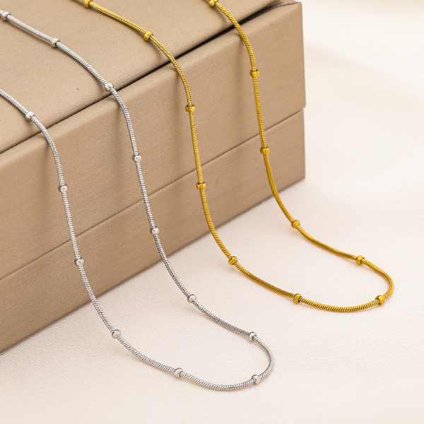 TCUBO%Y$~(CEZ`S0XX@MO Wholesale finished silver and 18K gold plated stainless steel satellite snake chain necklaces displayed elegantly side by side over a luxury jewelry box.