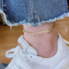 双层不锈钢扁蛇骨链+夹珠圆蛇链 (3) Model wearing a gold double layer stainless steel herringbone flat snake anklet around the ankle paired with white sneakers for summer style.