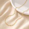 A delicate finished 18K gold plated stainless steel lip chain necklace draped gracefully on a white ceramic plate highlighting the mirror glimmer.