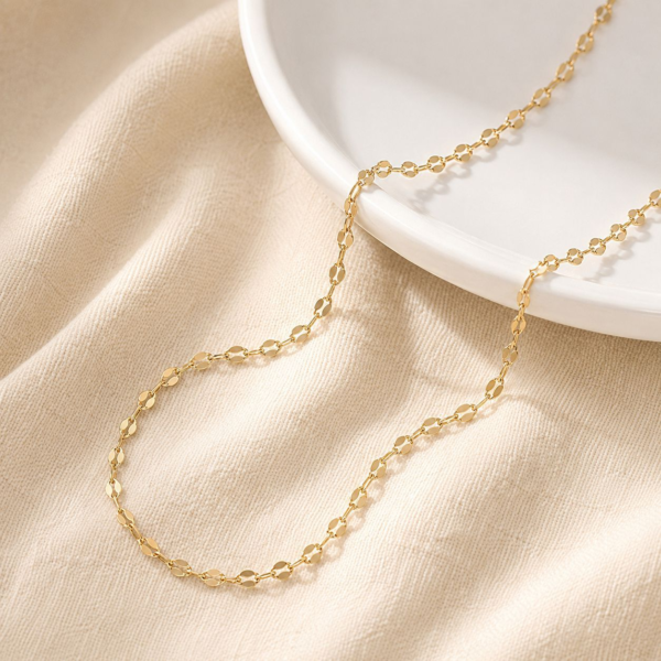 A delicate finished 18K gold plated stainless steel lip chain necklace draped gracefully on a white ceramic plate highlighting the mirror glimmer.