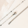 A silver stainless steel lip chain lies flat against a white background, showcasing its structure and details, including a lobster clasp, an extender chain, and a small metal tag.