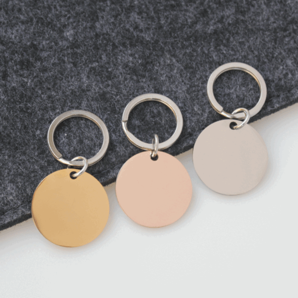 圆形钥匙扣 (1) Wholesale blank round disc stainless steel keychains in gold, rose gold, and silver finishes arranged neatly on a dark felt background for B2B supplier.