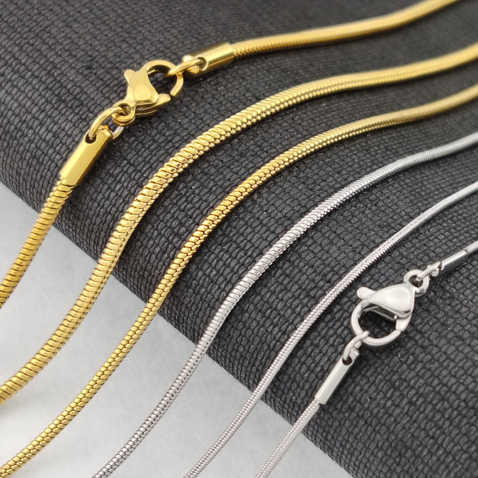 圆蛇链 (1) Close-up of multiple silver and gold stainless steel round snake chains side by side highlighting the premium lobster clasps and smooth texture.