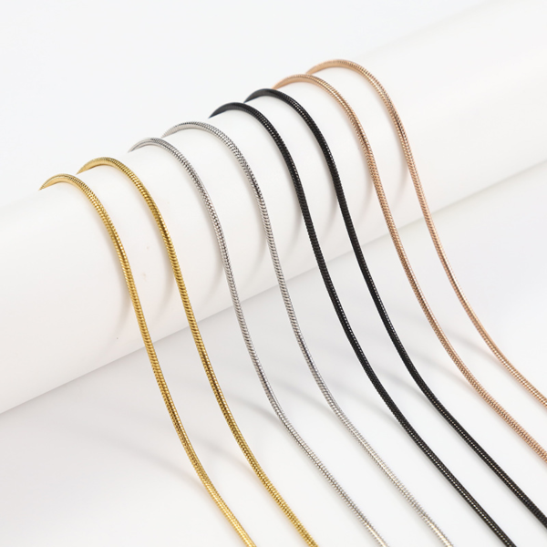 圆蛇链 (9) Wholesale finished stainless steel snake chain necklaces in gold, mirror silver, and matte black draped fluidly over a white cylindrical stage.