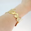 大字母手镯_0004_图层 3 Model wearing a personalized 18K gold plated stainless steel script name bangle on a wrist to showcase the smooth laser-cut lettering.
