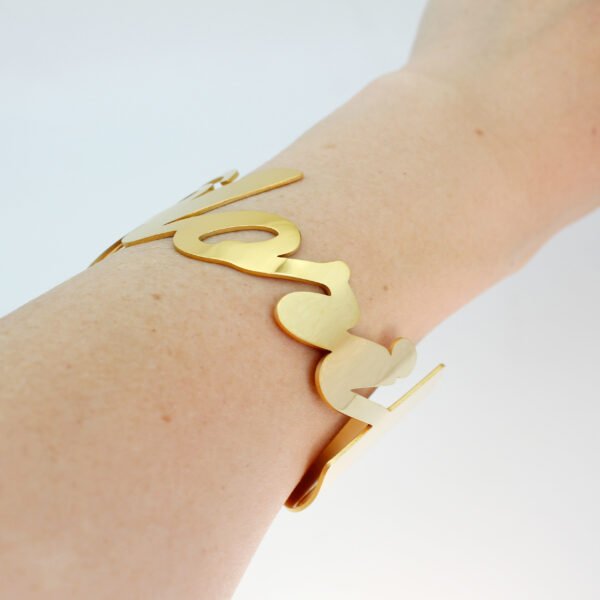 大字母手镯_0004_图层 3 Model wearing a personalized 18K gold plated stainless steel script name bangle on a wrist to showcase the smooth laser-cut lettering.