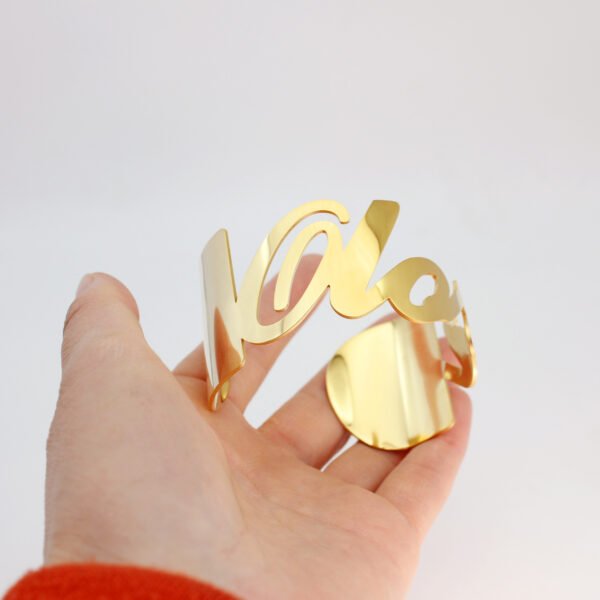 大字母手镯_0005_图层 2 Model wearing a personalized 18K gold plated stainless steel script name bangle on a wrist to showcase the smooth laser-cut lettering.