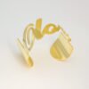 大字母手镯_0006_图层 1 Personalized cursive nameplate open cuff bracelet in luxury gold stainless steel standing flat on a white surface for custom jewelry store.