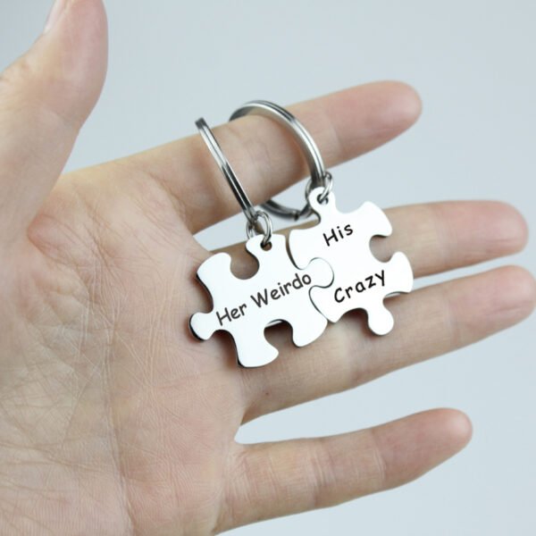 拼图钥匙扣 (6) A close-up view of fingers holding a pair of interlocking stainless steel puzzle keychains showing the precise seamless snapping mechanism.