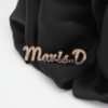 满钻字母胸针 (7) Wholesale personalized rose gold plated stainless steel rhinestone name brooch pinned on a black fabric background for premium retail display.