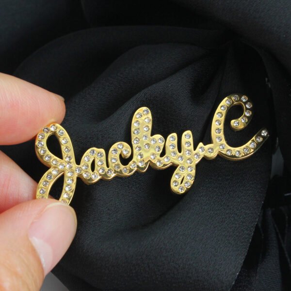 满钻字母胸针 (8) A hand holds a gold, fully stone-encrusted lapel pin featuring a custom-made name in script, showcasing its substantial thickness and the sparkling facets of the zirconia stones.