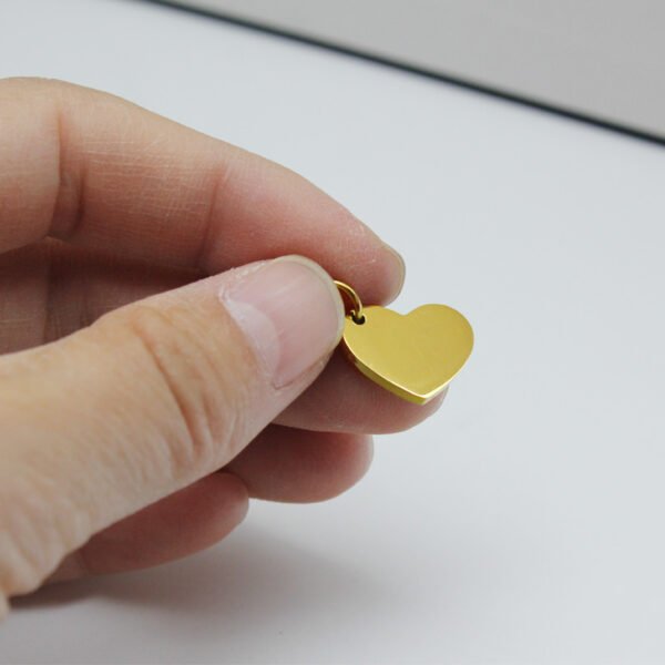 16×12偏孔小心形_0005_图层 1 A close-up view of fingers holding a mini 18K gold plated stainless steel heart tag blank to showcase its compact size and smooth edges.