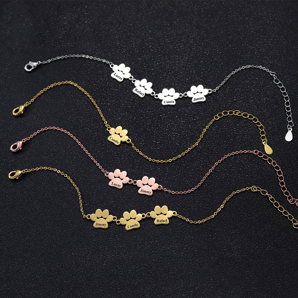 B2B catalog photo showing multiple finished stainless steel paw name bracelets in silver, gold, and rose gold with 1 to 4 customizable linked charms.