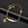 儿童刻字手链 (2) A finished gold plated stainless steel baby ID bar bracelet with a small butterfly charm and lobster clasp configuration on a black leather layout.
