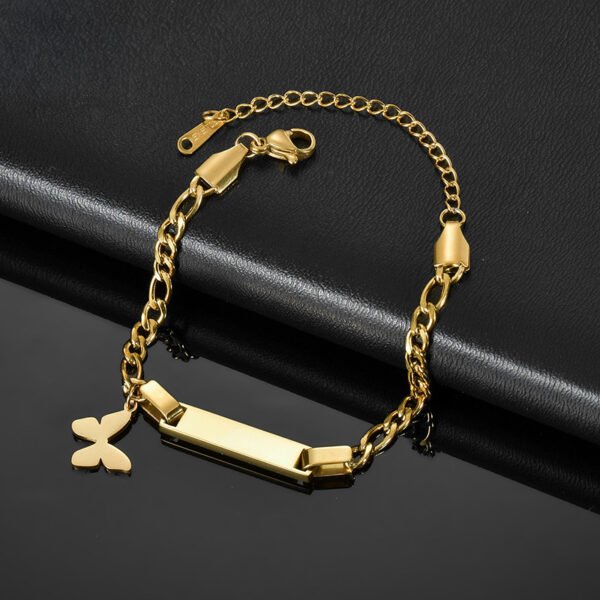 儿童刻字手链 (2) A finished gold plated stainless steel baby ID bar bracelet with a small butterfly charm and lobster clasp configuration on a black leather layout.