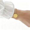 圆形18手链1000_0000_纯白图处理 Model wearing a sleek gold stainless steel round disc charm bracelet on a wrist paired with a white ruffled sleeve for premium boutique display.