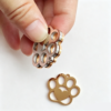 A close-up view of fingers holding three stacked stainless steel paw charms to highlight the heavy-duty metal thickness and smoothly polished beveled edges.