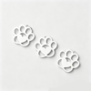Three blank finished silver stainless steel hollow paw shape charms laid flat in a diagonal row on a clean white background for B2B shop catalog.