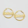 描边项链耳环套装_0001_图层 12 A pair of wholesale personalized 18K gold plated stainless steel circular hoop name earrings custom laser cut-out with script text "Anikeade" flatly laid.