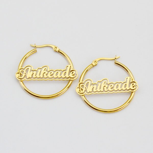 描边项链耳环套装_0001_图层 12 A pair of wholesale personalized 18K gold plated stainless steel circular hoop name earrings custom laser cut-out with script text "Anikeade" flatly laid.