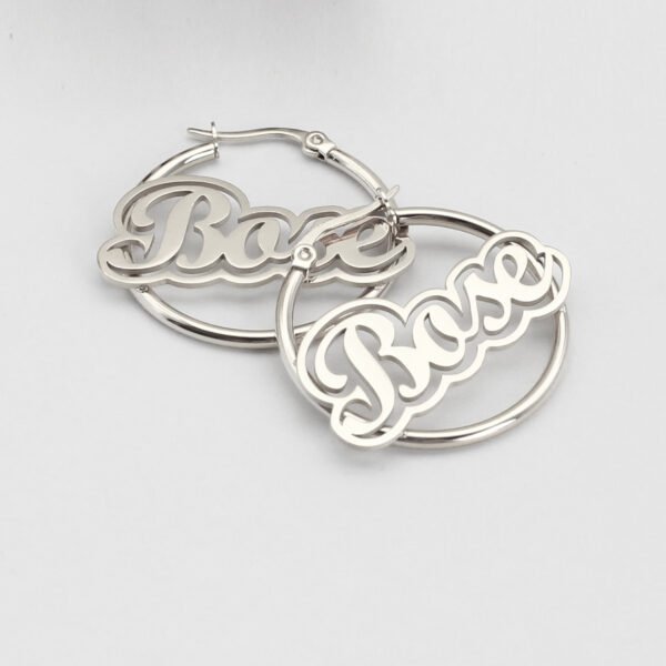 描边项链耳环套装_0007_图层 15 A close-up view of a pair of finished silver stainless steel circular loop name earrings custom etched with the script lettering "Bose" on a white backdrop.