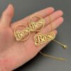 描边项链耳环套装_0011_图层 5 副本 A hand holding a wholesale custom 18K gold plated 3D script name necklace and matching hoop earrings to highlight their premium metal weight and luxury sheen.