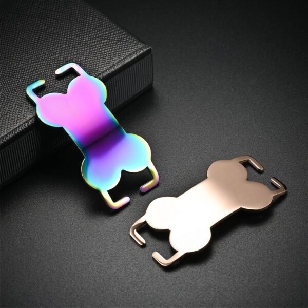 A rainbow anodized and a rose gold stainless steel slide-on collar tag leaning against a textured black box, showing the smooth curved edge profile.