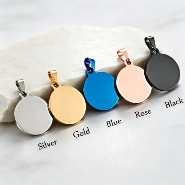 Five stainless steel round tags with attached pinch bails aligned on a white stone block, showing Silver, Gold, Blue, Rose Gold, and Black PVD finishes.