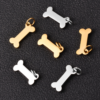 An assortment of small silver and gold stainless steel bone charms with mini jump rings displayed on a textured dark grey leather-like background.