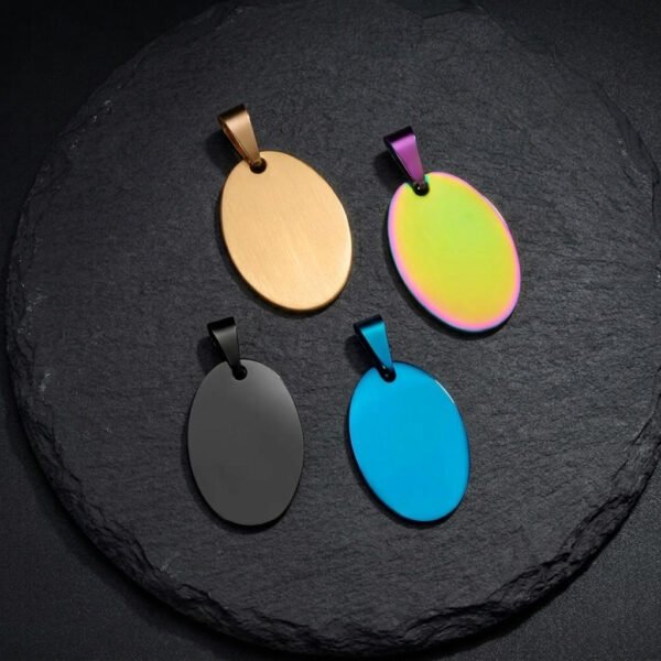 Top view of four polished oval metal tag blanks in gold, black, blue, and rainbow colors placed on a textured black slate stone background.