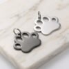 Brushed finish black and silver stainless steel paw print charms with split rings on a white marble background.