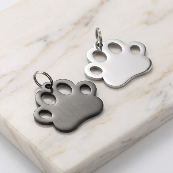 Brushed finish black and silver stainless steel paw print charms with split rings on a white marble background.
