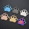 Assorted colorful laser-engravable stainless steel dog tags in paw shapes displayed on a dark grey textured surface.