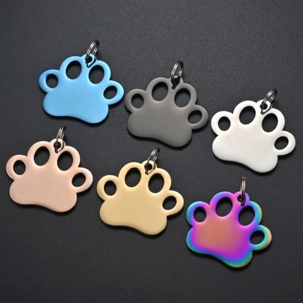 Assorted colorful laser-engravable stainless steel dog tags in paw shapes displayed on a dark grey textured surface.