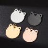 Four high-shine stainless steel cat charms in silver, black, gold, and rose gold, catching bright sunlight on a black matte tabletop.