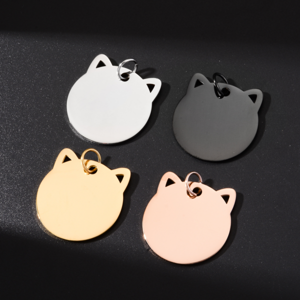 Four high-shine stainless steel cat charms in silver, black, gold, and rose gold, catching bright sunlight on a black matte tabletop.