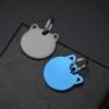 A matte black and a royal blue electroplated stainless steel cat shape tag, positioned overlapping on the corner of a textured box.