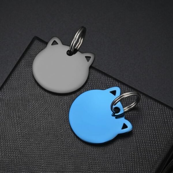 A matte black and a royal blue electroplated stainless steel cat shape tag, positioned overlapping on the corner of a textured box.