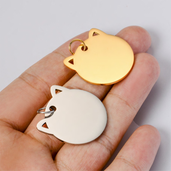 A person holding a silver and a gold stainless steel cat tag in their hand, showcasing the real-life 28x28mm size and precision cutout ear details.