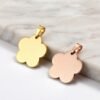 Two polished stainless steel flower pendant charms in gold and rose gold finishes, leaning on a light-colored smooth marble step.