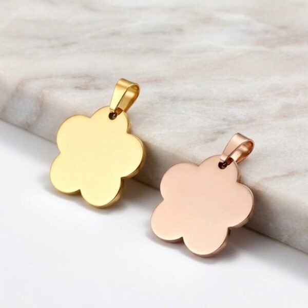 Two polished stainless steel flower pendant charms in gold and rose gold finishes, leaning on a light-colored smooth marble step.