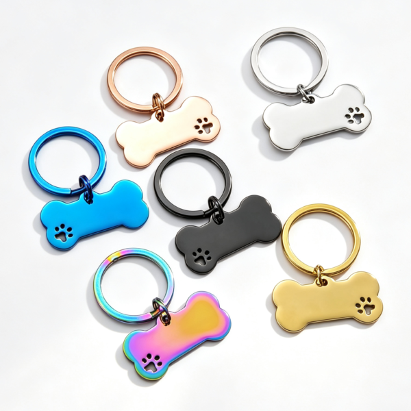 Six stainless steel dog bone tags with flat split keyrings and a cutout paw print accent, displayed in rose gold, silver, blue, black, gold, and rainbow finishes.