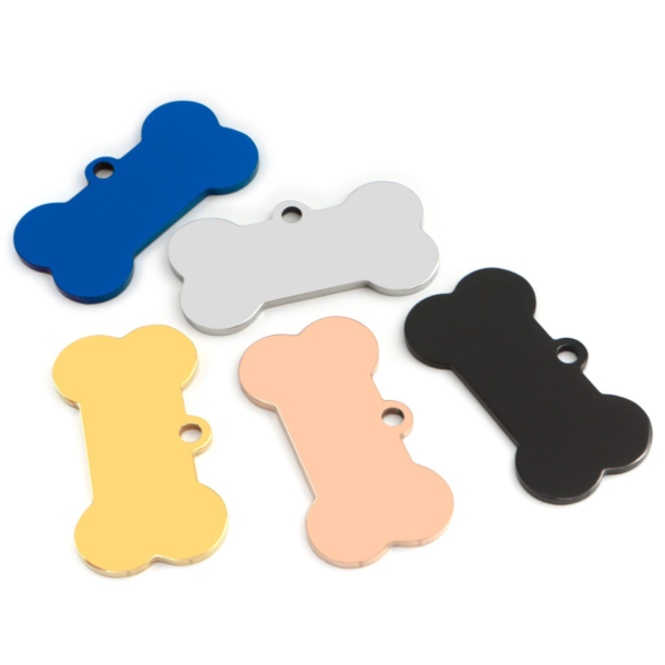 Blank metal dog bone tags with integrated hanging holes scattered on a white background in blue, silver, black, gold, and rose gold.